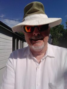 Man in direct sunlight wearing a wide-brimmed hat, sunglasses, and light weight clothing.